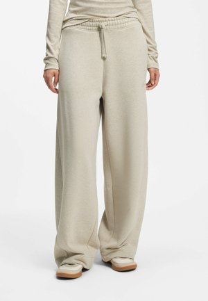 Beige vidde sweatpants med snøre i taljen, båret med matchende beige langærmet top og hvide sneakers med brune såler.