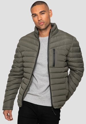 Veste en nylon matelassée zippée de couleur vert olive, avec un col montant, un quilting horizontal, une poche zippée et des accents noirs le long des coutures.