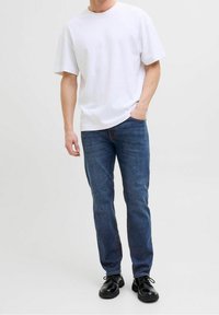 Camiseta blanca de algodón con mangas cortas combinada con jeans de mezclilla azul. Zapatos negros con cordones completan el conjunto. Diseño simple y casual.