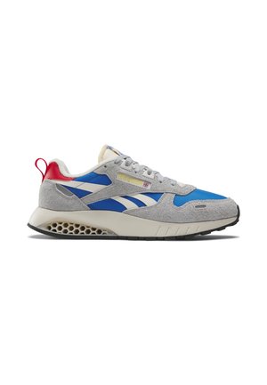 Tenisky Reebok s modrou textilií, šedými semišovými překryvy, bílou mezipodešví s designem včelí plástve, červenou patní částí a bílým logem Reebok na boku.
