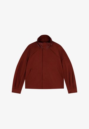 Veste rouge courte en tissu avec un col haut et des manches raglan. Elle présente deux poches avant et une finition de col contrastante lisse.