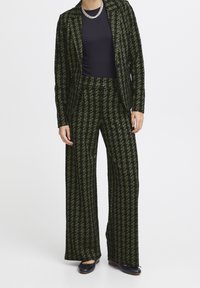 Completo a quadretti verdi e neri con blazer aderente e pantaloni a gamba larga, caratterizzato da una texture liscia e un motivo sottile a pied de poule.