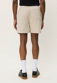Pantalones cortos beige hasta la rodilla, hechos de un tejido ligero, con una cinturilla elástica y dos bolsillos traseros con una sutil textura de rejilla.