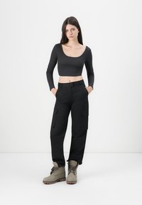 Top scurt negru cu mânecă lungă, asortat cu pantaloni cargo negri cu buzunare laterale. Botine gri până la gleznă cu un finisaj texturat. Design simplu, modern.