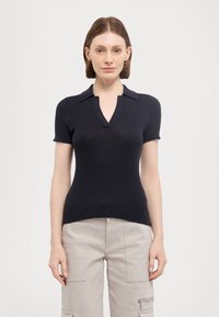 Marinblå ribbet polo-skjorte med korte ermer, V-hals og klassisk krage. Myk tekstur med en tettsittende design og sidesplitt ved kanten.