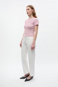 Rot-weiß gestreiftes kurzärmeliges T-Shirt, kombiniert mit weißen geraden Hosen und schwarzen spitzen Ballerinas vor einem neutralen Hintergrund.