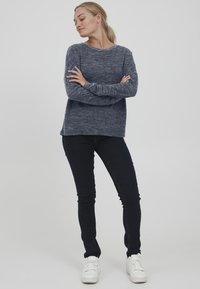 Marineblå teksturert genser med lange ermer og rund hals, kombinert med mørke jeans og hvite sneakers, som skaper et uformelt antrekk.