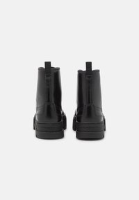 Botas negras hasta el tobillo hechas de material sintético brillante, con una suela texturizada, lengüetas y costuras reforzadas a lo largo de los lados.