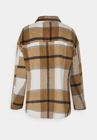 Ruskea ja kermaruudullinen takki, joka on valmistettu pehmeästä kankaasta, sisältäen kauluksen, pitkät hihat ja suoran helman. Huomiota herättäviä mustia yksityiskohtia.