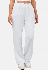 Witte, losse broek van textuurstof met een elastische tailleband en zijzakken, gestyled met witte sneakers.