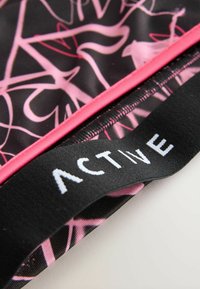 Schwarzer Stoff mit rosa abstrakten Mustern und rosa Besatz. Der schwarze Bund zeigt das Wort "ACTIVE" in weißen Buchstaben.