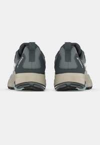 Graue Sportschuhe mit einer robusten beigen Sohle, die eine glatte Textur, verstärkte Ferse und eine Lasche zum einfachen An- und Ausziehen aufweisen.