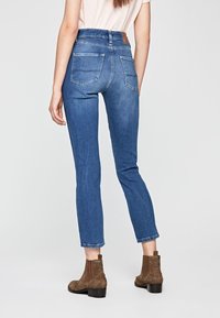 Högmidjade blå jeans med en ren design, smalnande ben och två bakfickor. Bärs med bruna ankelstövlar med klack.