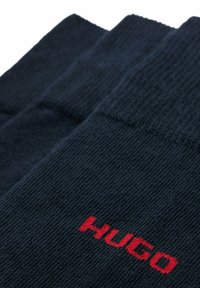 Marineblaue Socken aus strukturiertem Stoff, mit einem geriffelten Design und einem roten "HUGO"-Logo, das nahe dem Bündchen gestickt ist.