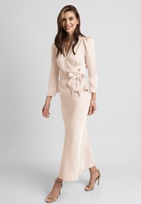 Sukienka wrap w jasno brzoskwiniowym materiale, z długimi rękawami, detalem w postaci wiązania w talii oraz zwiewną sylwetką sięgającą do podłogi.