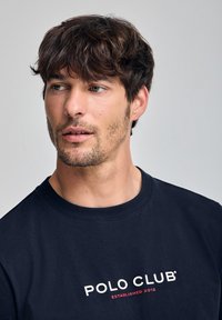 Mörkblå sweatshirt med rund halsringning, i bomullsmaterial, och en vit och röd "POLO CLUB ESTABLISHED 2012" logotyp på bröstet.