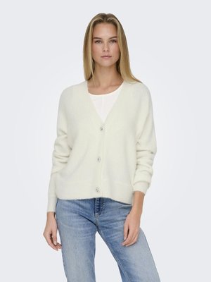 Cardigan bianco in maglia con scollo a V, bottoni frontali e orlo a costine. Indossato sopra una maglietta chiara e abbinato a jeans blu. Texture liscia.