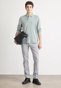 Light green long-sleeve polo shirt with ribbed texture, gray slim-fit pants, and black sneakers. A black bag is held under the arm.