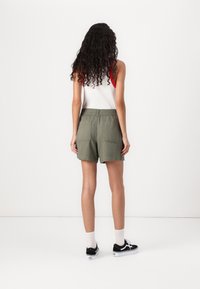 Olivgrön, knälånga shorts med elastisk midja och två bakfickor, kombinerat med svarta skor och vita strumpor.