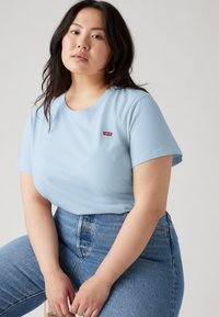 T-shirt bleu clair à manches courtes avec un col rond et un petit logo rouge Levi's. Associé à un jean en denim bleu taille haute.