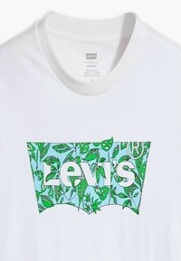 Camiseta de algodón blanca con un diseño de logo en forma de hojas en azul y verde que dice "Levi's" en letras blancas en negrita. Cuello redondo.