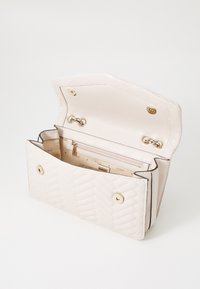 Quiltet beige taske med guldsmykker og knaplukning. Indersiden har en lynlåslomme og to rum med 'GUESS' branding.