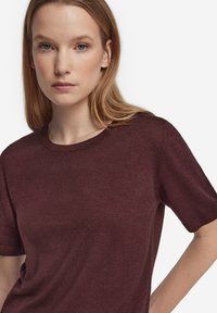 Vinröd kortärmad stickad topp med rund halsringning. Tyget verkar mjukt med en subtil textur; har en avslappnad passform och standardärmar.