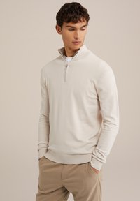 Svetlo bež pulover s četrtinskim zadrgo iz mehkega pletenega materiala. Ima rebrast ovratnik in manšete, sproščen kroj ter minimalne oblikovalske detajle.