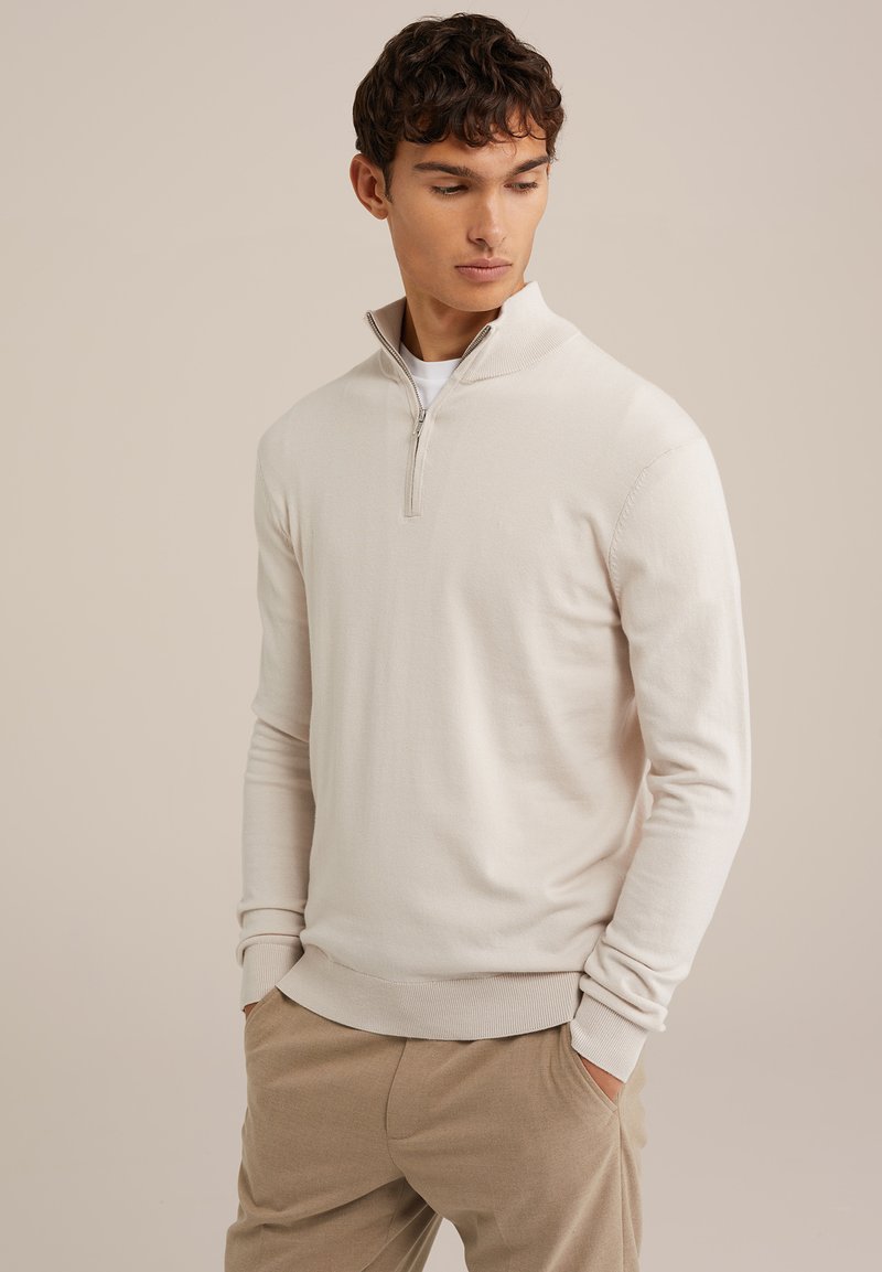 Svetlo bež pulover s četrtinskim zadrgo iz mehkega pletenega materiala. Ima rebrast ovratnik in manšete, sproščen kroj ter minimalne oblikovalske detajle.