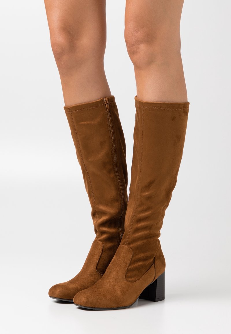 Bruna mockaskinn knähöga stövlar med en kraftig klack, med dragkedjestängning på sidan och en åtsittande design som smalnar av framtill.