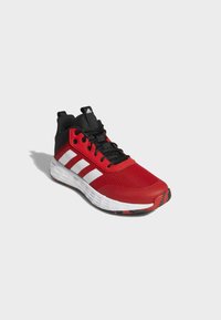 Zapatillas deportivas rojas con parte superior de malla, acentos negros, tres rayas blancas en el costado, cordones negros y suela de goma.