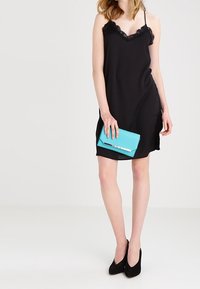 Czarna sukienka na ramiączkach z koronkowym wykończeniem, zestawiona z turkusową kopertówką i czarnymi szpilkami, o gładkim wykończeniu i luźnym kroju.