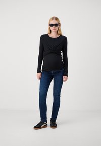 Top negro de manga larga con superficie de canalé y un frente torcido, combinado con jeans oscuros de corte ajustado y zapatillas negras con suelas de goma.