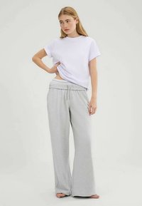 Weißes Baumwoll-T-Shirt mit hochgekrempelten Ärmeln, kombiniert mit hellgrauen, weit geschnittenen Jogginghosen mit elastischem Bund und Kordelzug.