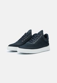 Paire de baskets basses noires avec dessus en cuir, lacets noirs et semelles épaisses en caoutchouc blanc sur fond uni.