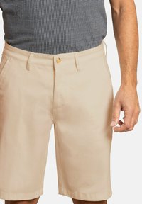 Pantalones cortos beige hechos de tejido ligero, con cierre de botón en la parte frontal, trabillas para cinturón y bolsillos laterales, con un corte recto por encima de la rodilla.