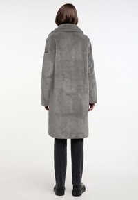 Grijze faux fur jas met een geknipt kraag, lange mouwen en een rechte snit, die tot halverwege het bovenbeen reikt, gecombineerd met zwarte broeken.