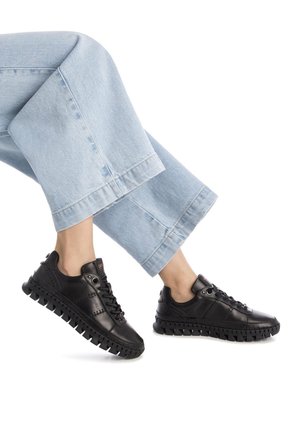 Las zapatillas negras cuentan con una parte superior de cuero suave, una suela de goma texturizada con surcos pronunciados y un diseño con cordones. Combinadas con unos vaqueros de pierna ancha en azul claro.