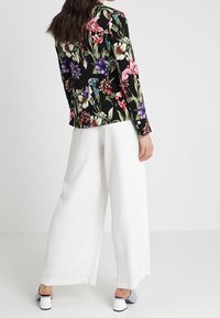 Zwart blazer met bloemmotief in levendige kleuren, gecombineerd met witte wijde broek. Heeft lange mouwen en knoopaccenten.