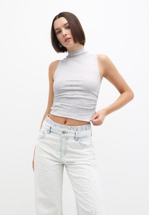 Hellgrau, ärmelloses Oberteil mit Stehkragen, kombiniert mit hochtaillierten, strukturierten, hellblauen Jeans. Die Jeans verfügen über einen elastischen Bund.