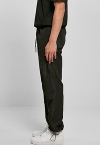 Pantalones negros con cordón, confeccionados en tejido ligero, que presentan un corte relajado. Combinados con zapatillas blancas, que destacan el diseño de pernera ajustada.