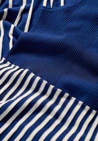 Tissu bleu côtelé avec des rayures blanches, présentant une texture lisse et des largeurs de rayures variées. Sections de motifs unis et rayés présentes.