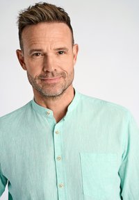 Camicia button-up verde menta con colletto, tasca sul petto e tessuto texturizzato. Presenta bottoni di colore chiaro e un design a vestibilità rilassata.