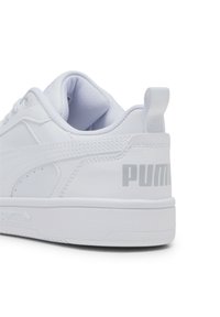 Baskets blanches avec une tige en cuir lisse, un col rembourré et une semelle en caoutchouc texturée. Marque "PUMA" grise sur le talon.