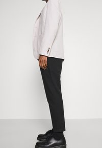 Blazer de lino gris claro con dos botones, pantalones negros ajustados y zapatos negros con cordones, con una textura suave y un corte entallado.