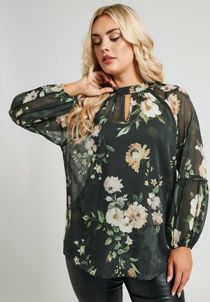 Blusa nera trasparente con stampe floreali in crema e verde. Presenta un collo a chiave e maniche a sbuffo con polsini elasticizzati. Tessuto morbido.