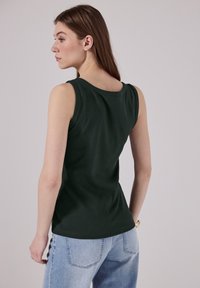 Top senza maniche di un verde scuro con scollatura rotonda, realizzato in tessuto morbido; abbinato a jeans a vita alta di un blu chiaro. Tessuto liscio e design aderente.