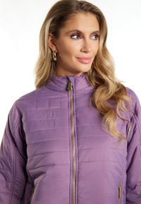 Giacca a vento viola con colletto alto, chiusura con zip e cuciture orizzontali. Presenta dettagli in hardware dorato e una texture liscia e lucida.