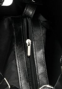 Interno di una borsa in pelle nera con chiusura a zip e texture liscia. Presenta un tirante della zip argentato e foderatura in tessuto nero.
