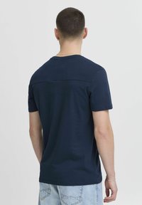 Tamsiai mėlyno medvilnės marškinėliai trumpomis rankovėmis, turintys glotnų tekstūrą ir tiesų kirpimą. Paprastas dizainas, be papildomų raštų ar akcentų.